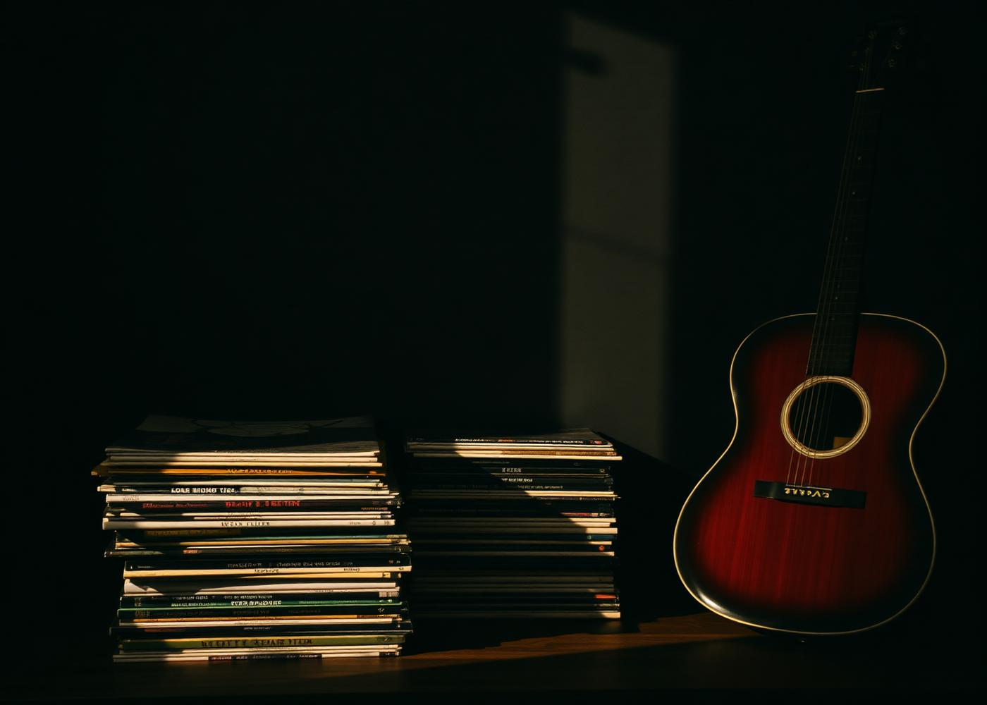 Stacked vinyl records and a guitar photographed in warm low light